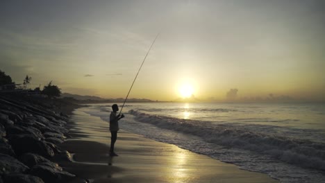 A-traditional-Indonesian-fisherman-fishing-on-a-coast-of-an-ocean-or-a-sea-at-Sunset-or-sunrise,-Slow-motion