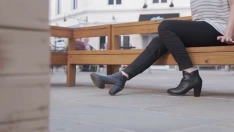 Slide-shot-set-in-a-French-styled-district-of-a-woman-wearing-black-jeans-and-black-designer-fashion-boots-sitting-on-a-wooden-bench
