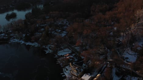 Drone-rise-over-lake-houses-and-forest-and-hills-at-sunrise-in-cold-winter