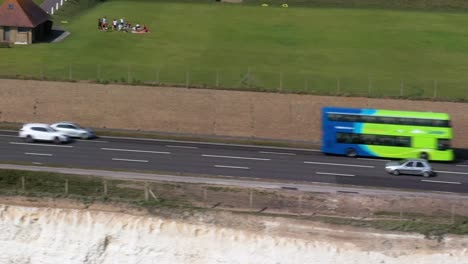 Aerial-tracking-shot-of-the-A259-coast-road-near-Brighton,-UK-with-infamous-Green-Brighton---Hove-buses-passing-through-the-frame
