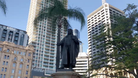Kameraschwenk-Thomas-Joseph-Ryan-Statue-Brisbane-Stadt-Mit-Hohen-Gebäuden-Und-Grünflächen