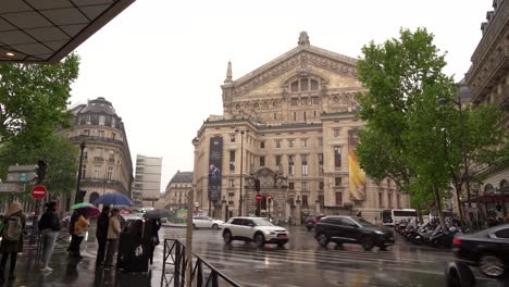 People-and-traffic-driving-in-front-of-Palais-Garnier,-an-opera-house-in-Paris