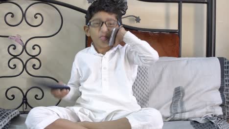 Cute-little-boy-child-funny-Mocking-making-faces-and-talking-on-phone-wearing-spectacles-glasses-television-remote-in-one-hand-front-view