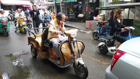 Xian,-China---August-2019-:-Man-sitting-in-his-rickshaw-and-talking-on-his-mobile-phone-on-the-busy-hectic-traffic-road-in-the-Muslim-Quarter,-Xian-Old-Town-town