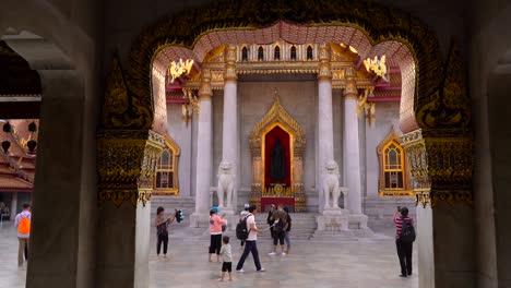 Bangkok,-Thailand,-Wat-Benchamabophit-Tempelfassade-Mit-An-Der-Wand-Montierter-Buddha-Statue-Mit-Goldenem-Randrahmen,-Daneben-Zwei-Aus-Marmor-Geformte-Löwenbilder-–-Mittlere-Aufnahme