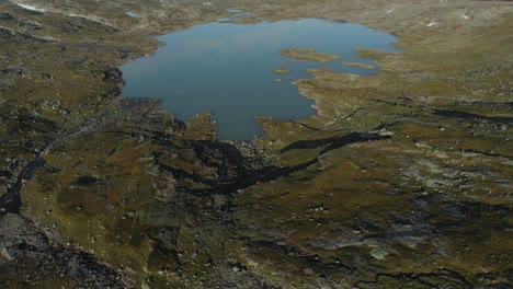 Hardangervidda-glacial-lake-with-glacier-in-background,-Norway,-aerial-reveal