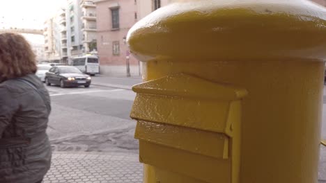 People-walk-by-yellow-mailbox-in-Seville,-Spain,-Closeup-on-letterbox