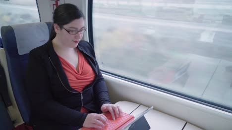 Young-woman-typing-on-long-distance-train-with-tablet-keyboard