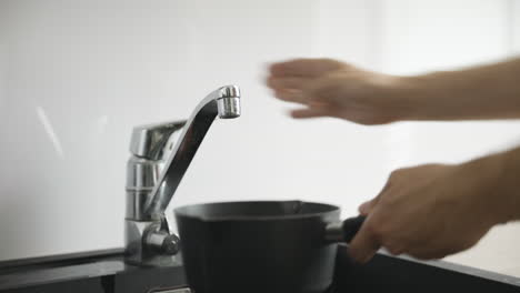 Close-view-of-male-hands-turning-on-faucet-and-filling-small-black-pot