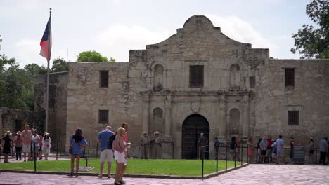 Mientras-La-Bandera-De-Texas-Ondea-Con-Una-Suave-Brisa,-Los-Turistas-Visitan-El-Famoso-E-Histórico-álamo-En-San-Antonio,-Texas