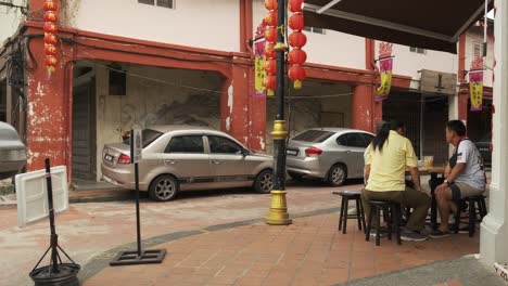 Wide-Angle-shot-of-chinese-family-eating-outdoors-near-sidewalk-at-cafe-in-Johor-Bahru,-Malaysia