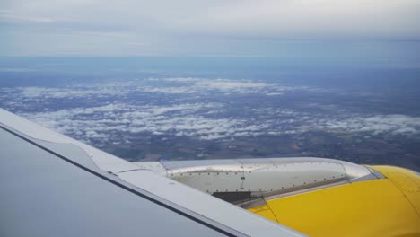 POV-airplane-passenger:-scenic-above-view-of-white-clouds-in-sky-and-horizon-with-view-of-aircraft-wing-and-yellow-engine-in-flight,-handheld-slow-motion
