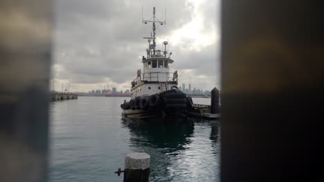 Push-in-of-tug-boat-docked-at-pier-through-waterfront-railing