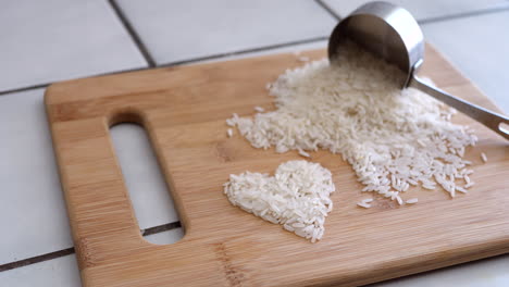 Weißes-Reiskorn-In-Einem-Herzen-Mit-Kochutensilien-Und-Messbecher-In-Einer-Küchenrutsche-Nach-Rechts