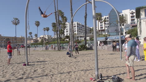 A-man-swinging-back-and-forth-on-the-traveling-rings-at-Santa-Monica-Beach-in-Los-Angeles,-California