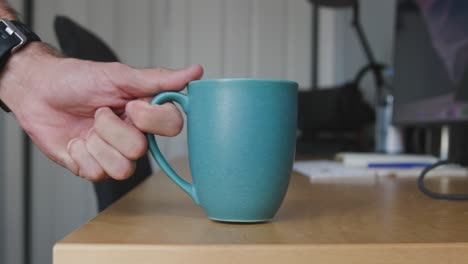 Eine-Kaffeetasse-Steht-Auf-Einem-Schreibtisch-Und-Wird-Von-Hand-Bewegt