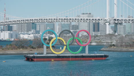 Olympic-Rings-Monument-Display-In-Odaiba-With-A-Panorama-Of-Rainbow-Bridge-Across-Tokyo-Bay-In-Minato,-Tokyo,-Japan