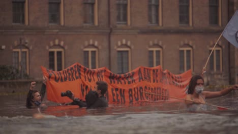 Activists-With-Banner-In-Water-To-Draw-Attention-on-climate-change-and-sea-level-rise-During-Extinction-Rebellion-Protest-In-front-of-parliament-The-Hague,-Netherlands---hofvijver,-slowmo