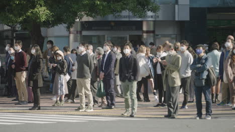 Während-Covid-19-In-Tokio,-Japan,-Fahren-Fahrzeuge-Auf-Der-Straße-Mit-Fußgängern-Mit-Gesichtsmaske,-Die-Darauf-Warten,-Die-Shibuya-Kreuzung-Zu-überqueren