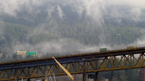 Timelapse-De-Movimiento-De-Vehículos-Y-Nubes-Por-El-Puente-Conmemorativo-De-Los-Herreros-En-Vancouver,-Bc,-Canadá-Con-Una-Exuberante-Montaña-Forestal-En-El-Fondo