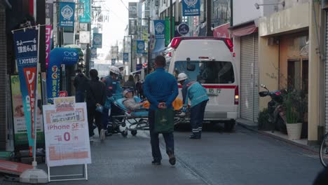 Socorristas-De-Primeros-Auxilios-Del-Departamento-De-Bomberos-De-Tokio-Llevando-A-Un-Paciente-En-Camilla-A-La-Ambulancia-El-Día-De-Año-Nuevo-En-La-Calle-De-Tokio,-Japón