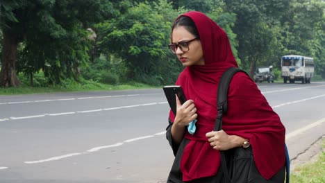 KOLKATA-,INDIA-:Young-Afghan-woman-holding-book-and-standing-alone-on-the-street-side,-waiting-for-taxi-or-public-transport-service-to-pick-up,-girl-with-expectation,background-bus,4k-video,transport