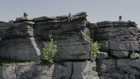 Climber-Sitting-On-Cliff-Looking-Down-On-His-Friend-Climbing-On-Bamford-Edge-In-England,-UK