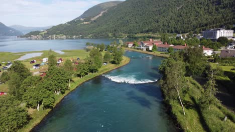 Antena-Estática-Sobre-El-Río-Loen-Con-Turistas-Acampando-En-El-Lado-Izquierdo-Y-Hoteles-Loenfjord-Y-Hotel-Alexandra-En-El-Fondo---Nordfjord-Noruega