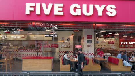 Fußgänger-Gehen-An-Der-Amerikanischen-Multinationalen-Fast-Food-Restaurantkette-Five-Guys-Und-Ihrem-Logo-Vorbei,-Während-Kunden-In-Dem-Restaurant-In-Hongkong-Essen