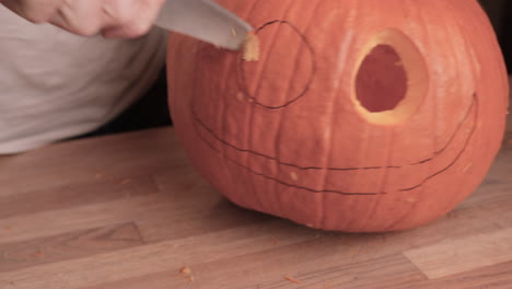 Man-Carved-Pumpkin-Head-Eyes-With-Knife-On-Wooden-Table