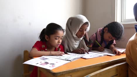 Three-Young-Muslim-Children-Reading-And-Writing-At-Desk-In-Classroom-In-Pakistan