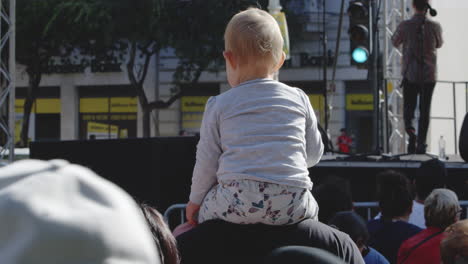 Toddler-sits-on-shoulders-of-father-at-concert-waiting-for-band-to-play