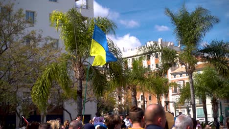 Ukrainian-flag-being-waved-high-above-crowds-during-protests-in-Malaga,-Spain