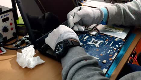 Gloved-Male-Hands-Working-On-Laptop-Motherboard-On-Desk