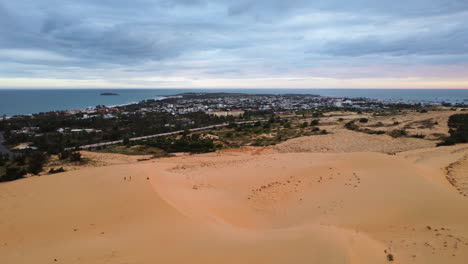 Aerial-sand-dunes-coastline-seascape-in-Mui-Ne-Vietnam,-drone-fly-above-little-fisherman-village-over-the-ocean-during-a-cloudy-day-revealing-scenic-landscape