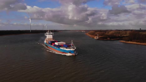 Greetje-Cargo-Ship-Navigating-Oude-Maas-With-Wind-Turbine-In-Background-Through-Barendrecht
