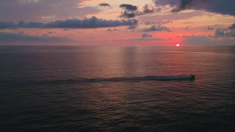 Luftaufnahme-Eines-Schnellboots,-Das-Auf-Dem-Meer-Segelt,-Mit-Einem-Wunderschönen-Filmischen-Sonnenuntergang-Am-Horizont