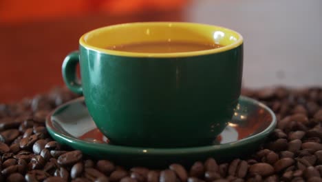 Pouring-milk-into-a-cup-of-coffee-which-is-beautiful-decorated,-standing-on-a-bunch-of-coffee-beans-and-in-a-nice-dark-and-light-green-cup