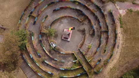 Aerial-top-down-circling-view-directly-above-artistic-creative-empty-colorful-labyrinth-with-wooden-structure-in-center