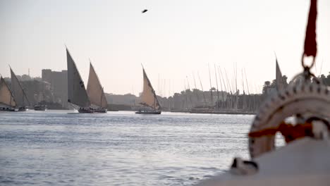 View-of-the-front-of-a-felucca-with-feluccas-sailing-in-the-backgroudn-during-golden-hour-on-the-Nile-river,-Aswan,-Egypt