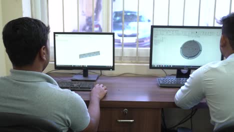Two-Computer-engineers-animating-a-3d-model-of-metal-object-in-3d-software-in-desktop-computer,-slow-zoom-in-shot
