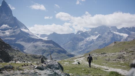 Schwarzer-Männlicher-Reisender-Mit-Rucksack,-Der-Sich-An-Einer-Klippe-Umschaut-Und-Die-Berglandschaft-In-Der-Nähe-Des-Matterhorns-In-Der-Schweiz-Erkundet