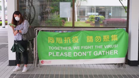 A-woman-stands-next-to-a-banner-that-reminds-the-public-to-avoid-gatherings-to-help-contain-the-spread-of-the-Coronavirus-variant-outbreak-in-Hong-Kong