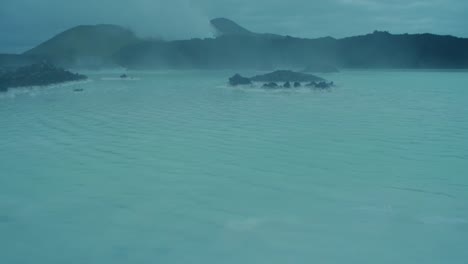Islandia,-Laguna-Azul,-Estación-De-Energía-Geotérmica-Svartsengi-En-La-Noche,-Niebla-Rodando-Sobre-El-Agua-Azul,-Movimiento-De-La-Cámara,-Inclinación-De-La-Cámara-Hacia-Arriba,-Toma-De-Lente-Gran-Angular