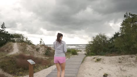 Young-woman-goes-on-wooden-path-to-beach-near-the-sea
