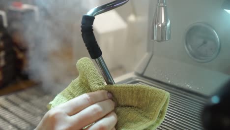 Professional-female-barista-cleans-steam-wand-with-cloth