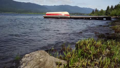 Small-waves-gently-lapping-on-shore-of-Lake-Quinault,-Washington,-a-floating-dock-and-a-boat-are-in-the-background