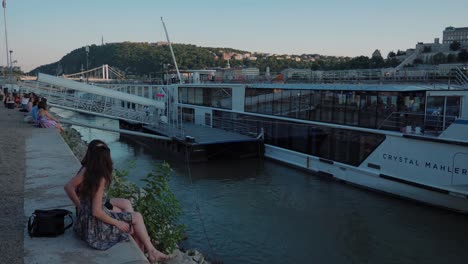 Danube-view-from-Raqpart-shore,-Pest-side,-girl-sitting-infront-of-river-cruise-Crystal-Mahler