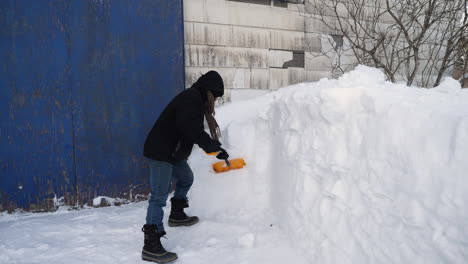 Man-shoveling-snow-off-snowbank-in-front-of-a-barn