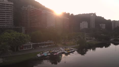 Sunrise-aerial-rotating-movement-showing-water-bikes-on-the-shore-of-the-city-lake-in-Rio-de-Janeiro-revealing-the-Corcovado-mountain-behind-the-residential-neighbourhood-mountain-range
